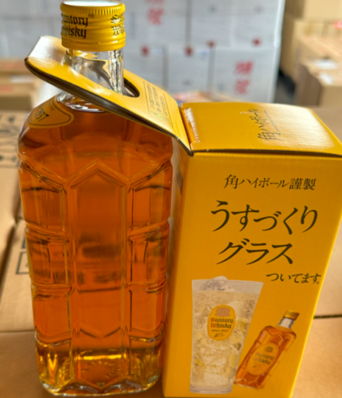 Bottle of whiskey with a yellow cap and packaging on a wooden surface.